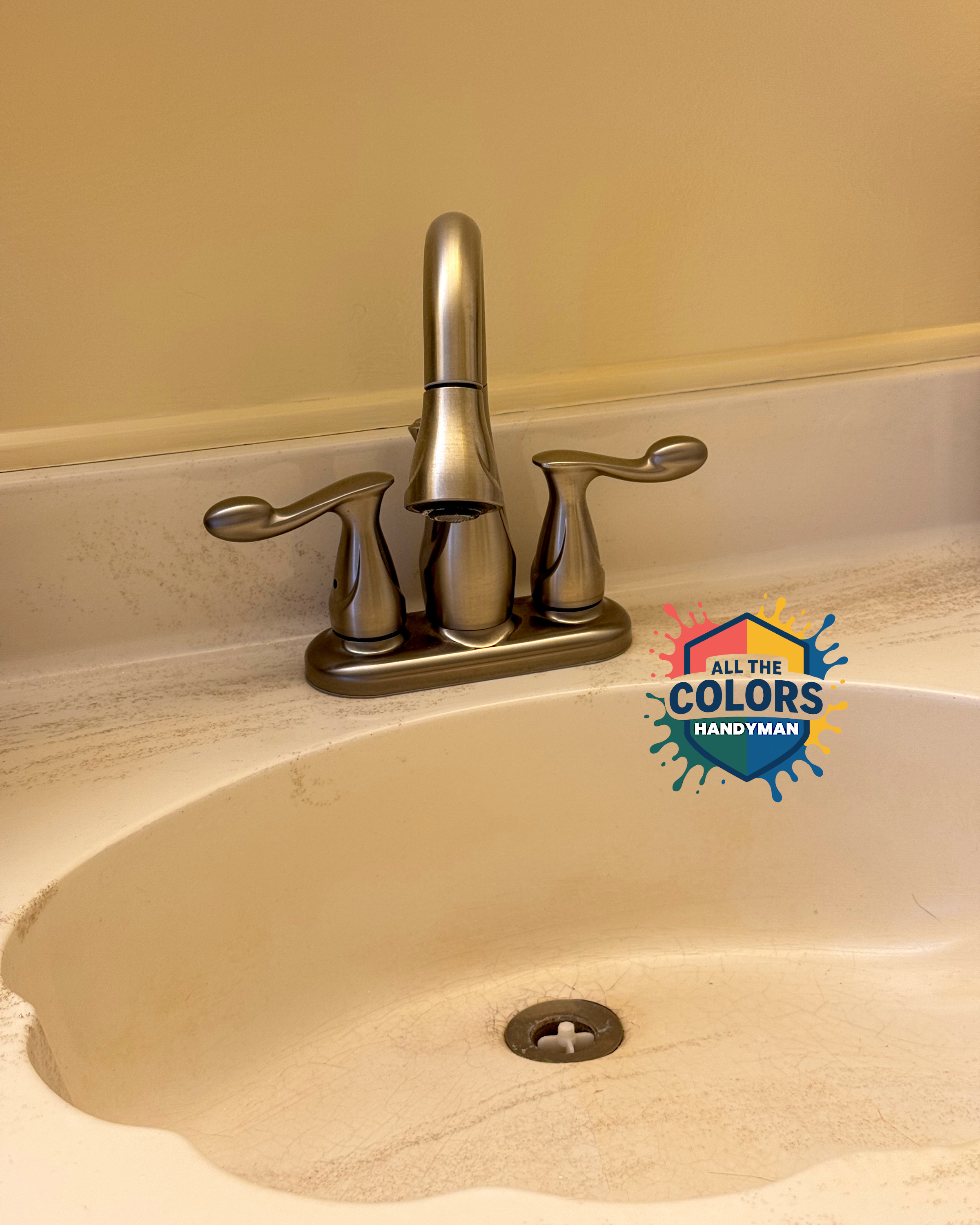 A faucet on an off-white vanity. It has swoopy, organic curves in a brushed nickel finish. A seam near the end indicates that the business end can be detached. The stopper is missing.